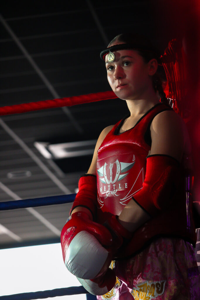 Une jeune boxeuse attend dans son coin. Elle regarde son adversaire, prête à se battre.